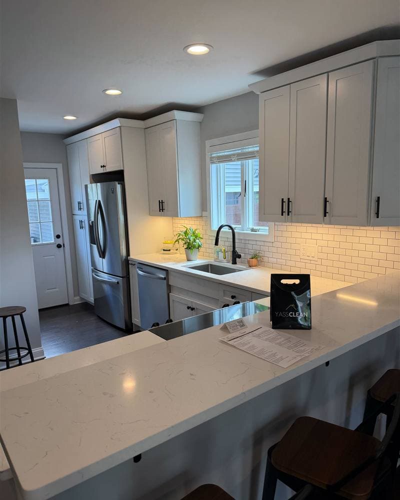 A bright, spotless modern kitchen with white cabinets and a YassClean bag on the counter.